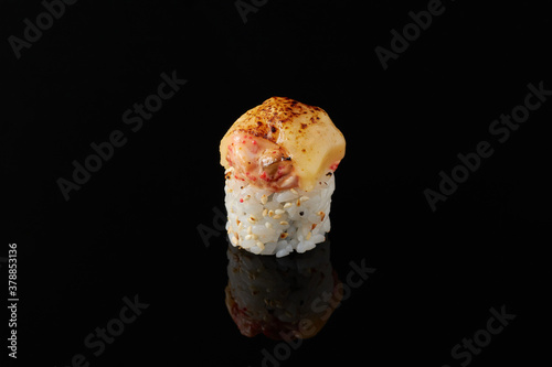 Maki - smoked eel, cream cheese, avocado, masago, sesame seeds, tempura, Spicy sauce on a black background
