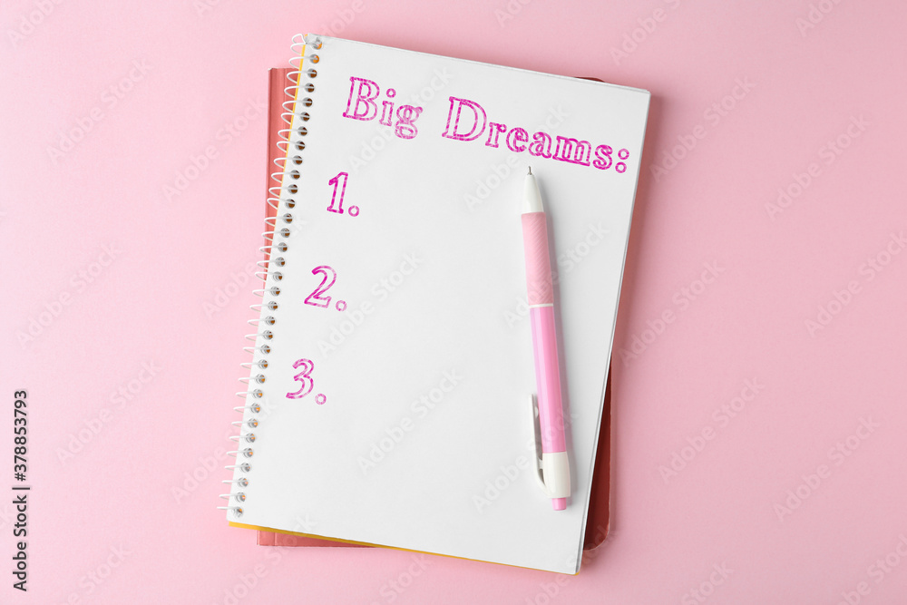 Notebook with dreams list and pen on pink table, top view