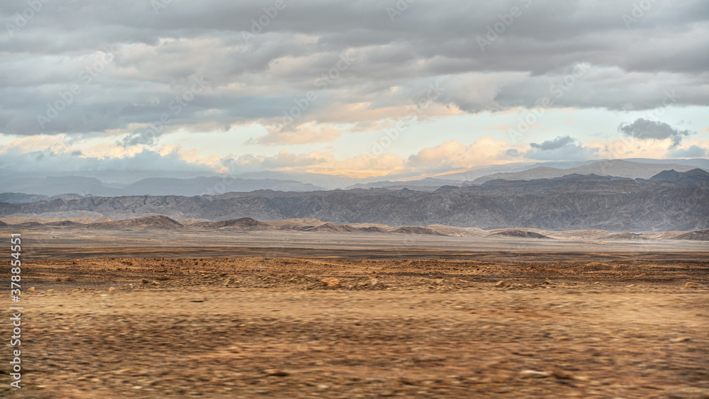 Typical landscape at Israel Jordan border as seen from car driving on Highway 90. Flat dry desert with small mountains at Jordanian side, sun shines through evening clouds