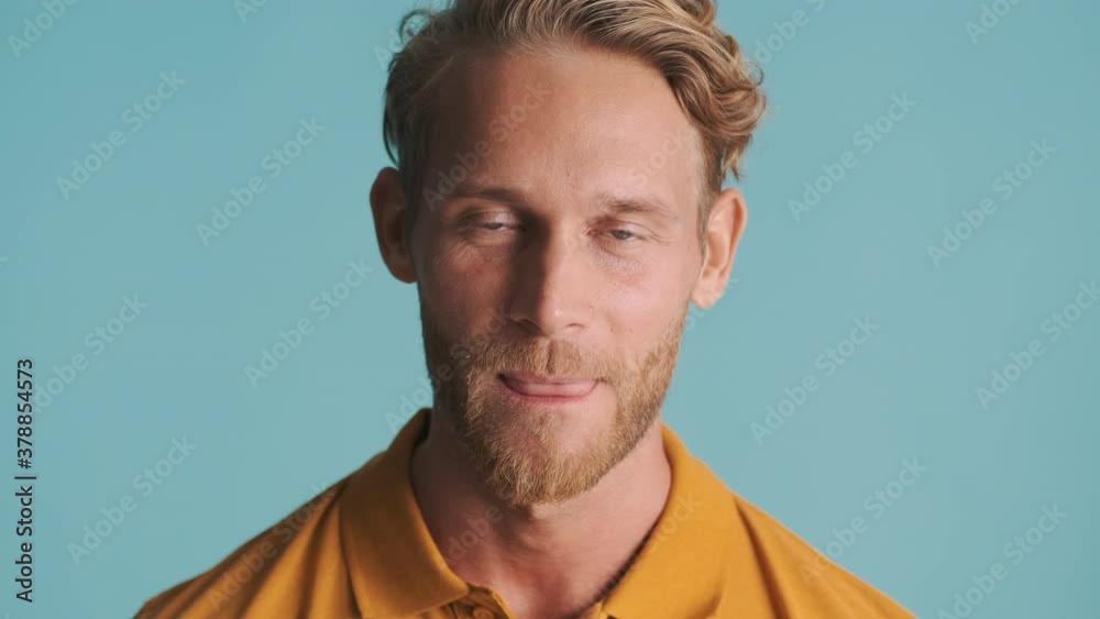 Young blond bearded man smiling and licking lip on camera over colorful background