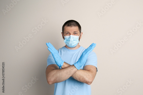 Man in protective mask showing stop gesture on beige background. Prevent spreading of COVID   19
