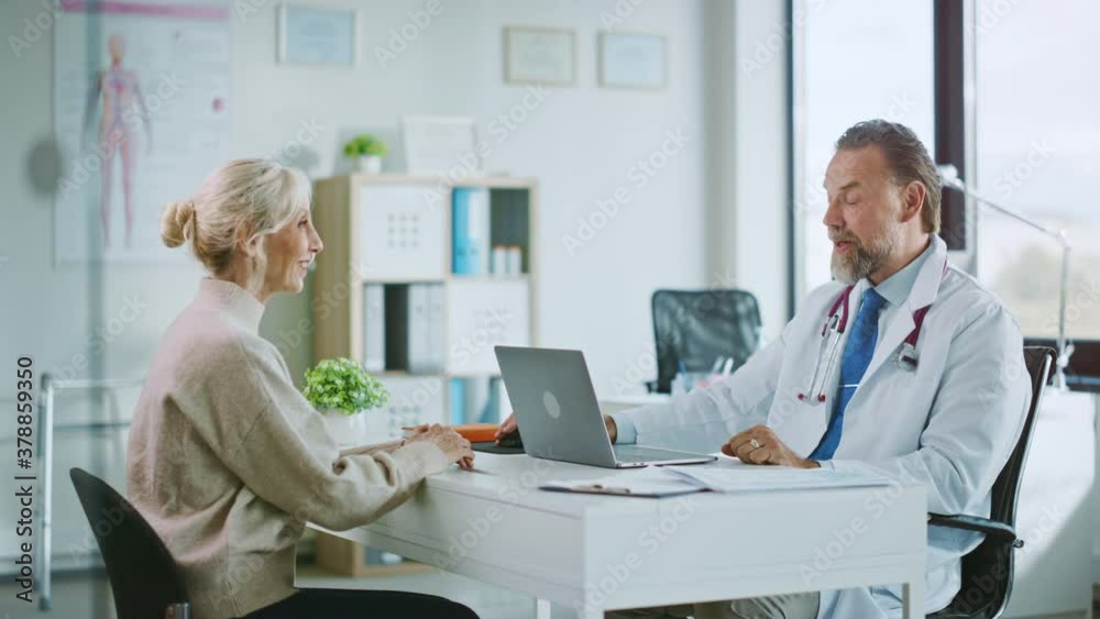 Friendly and Cheerful Family Doctor is Reading Medical History of Senior Female Patient During Consultation in a Health Clinic. Physician Using Laptop Computer in Hospital Office. Friendly and Cheerful Family Doctor is Reading Medical History of Senior Female Patient During Consultation in a Health Clinic. Physician Using Laptop Computer in Hospital Office.