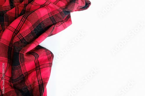Bright red plaid wrinkled shirt on a white background. Environment for working or studying from home. Empty surface surrounded by soft warm material. Cozy home office desk setting for isolation.