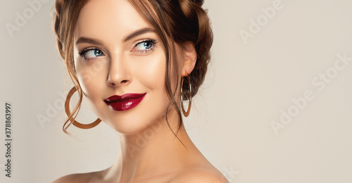 Beautiful model girl with burgundy or wine color lips  . Fashion makeup and cosmetics . Jewelry, earrings and accessories. Beauty woman with braid hairstyle around her head.