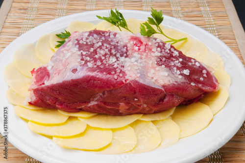Close-up of a raw steak on a bed of sliced potatoes marinated with rock salt