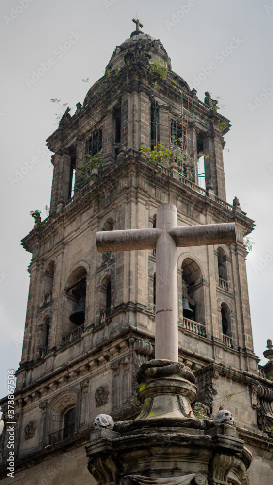 Bell Tower of the Cathedral of Mexico City Behind a Concrete Cross and Concrete Skulls