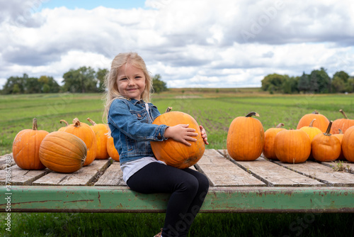 Fotografie Cute little girl choosing a pumpkin at the farm