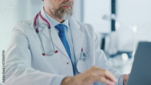 Wallpaper Mural Close Up of a Family Medical Doctor Working on a Laptop Computer in a Health Clinic. Physician in White Lab Coat is Browsing Medical History Behind a Desk in Hospital Office.  Torontodigital.ca