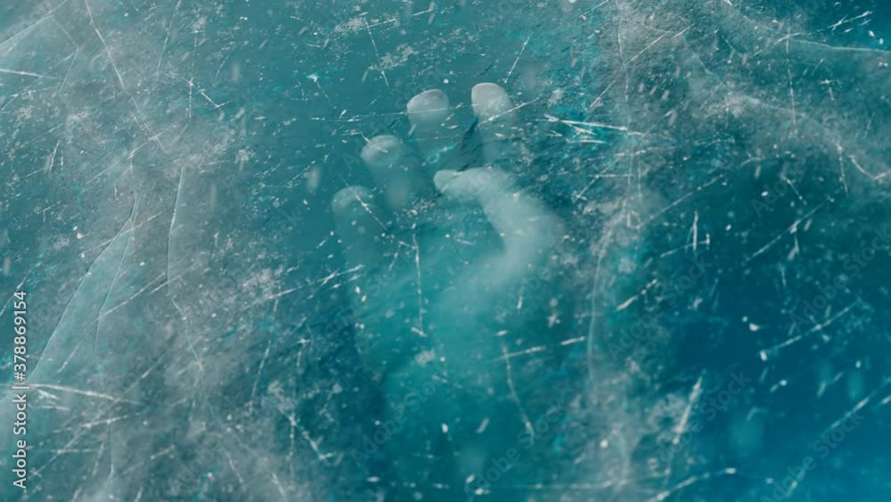 A human hand under the ice. The dead body is trapped underwater below the ice.