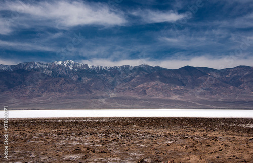 Death Valley National Park Salt flats in the foreground and cloudy sky and snowy mountain in the background in early Spring