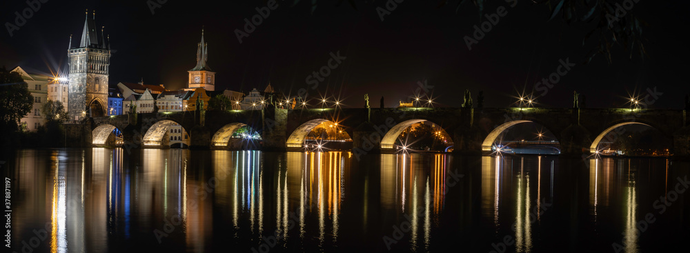 
illuminated Charles Bridge from the 14th century in the center of Prague on the Vltava river at night and street light and light reflections on the river surface