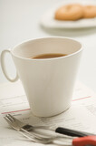 Close-up of a tea cup with two forks on a newspaper