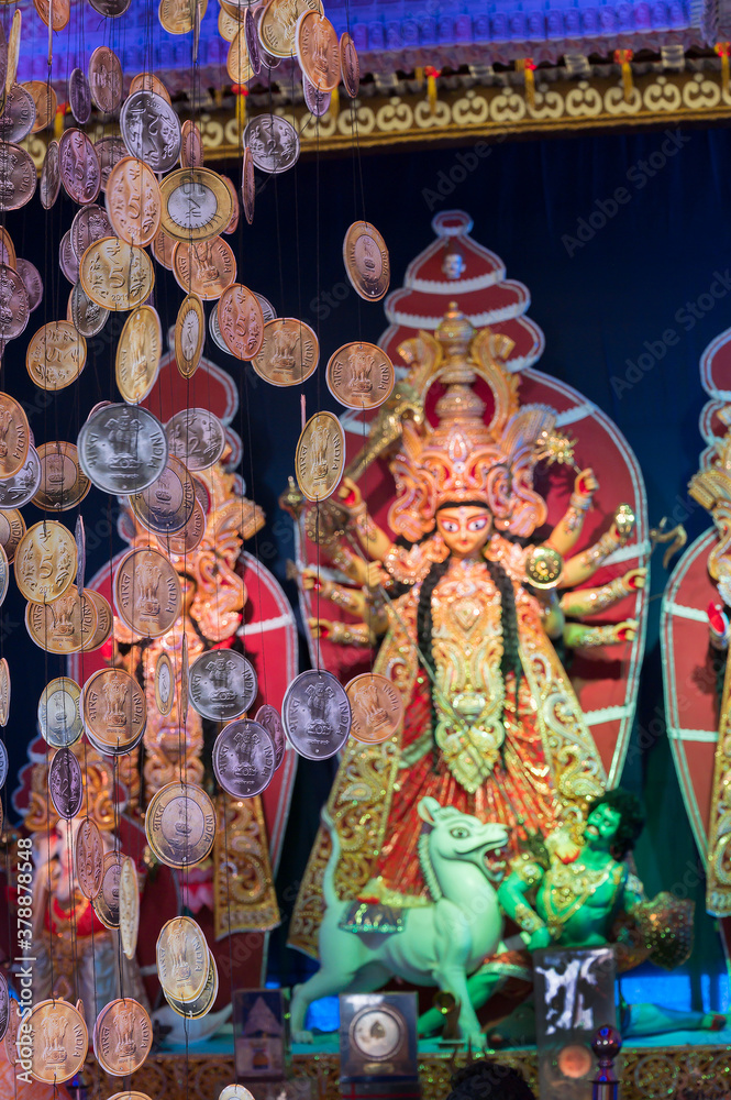 Decorated Durga Puja pandal with Durga idol, Out of focus hanging coins , Durga Puja festival at night. Shot under colored light.