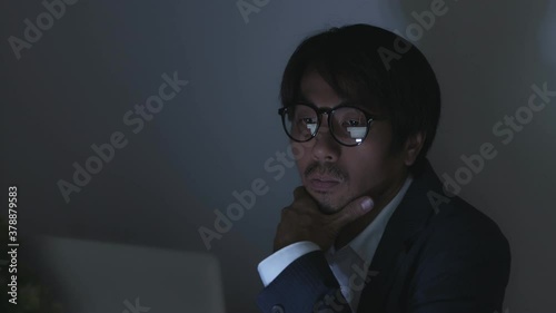Young Insurance Agent or Asian Businessman in Suit Wear Glasses Typing Laptop and Touch Chin Working Late or Night Work at Office in Truck Shot