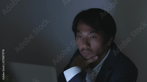 Young Insurance Agent or Asian Businessman in Suit Typing Laptop and Touch Chin Working Late or Night Work at Office in Truck Shot
