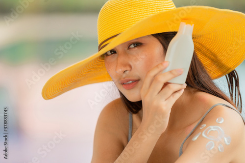 Attractive woman with healthy skin applying sunscreen on a sunny day and holding blank sunscreen UV protective lotion bottle packaging cosmetic template for your design.