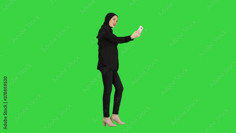 Young pretty muslim woman in hijab having video call on her phone as she walks on a Green Screen, Chroma Key. Young pretty muslim woman in hijab having video call on her phone as she walks on a Green Screen, Chroma Key.