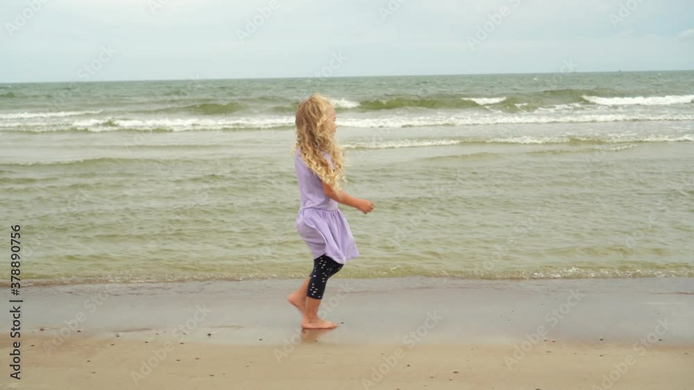 Gorgeous blond girl walking through sea shore. Lovely child with curly hair Gorgeous blond girl walking through sea shore. Lovely child with curly hair