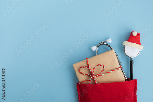 Medical stethoscope wearing hat with gift box in Santa Claus red bag. Christmas and New Year concept. Creative medical winter greeting card. Top view, flat lay, copy space