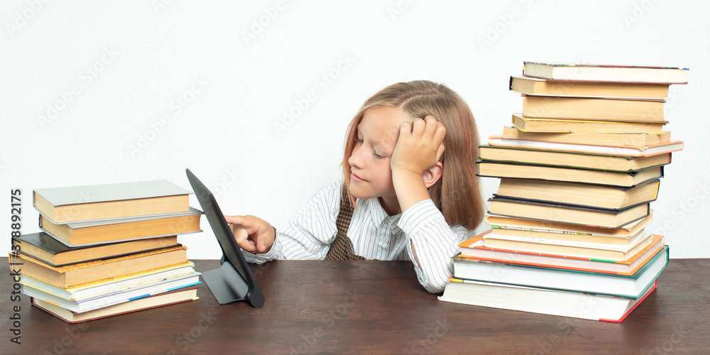 A teenage girl sits among books and uses a tablet. A teenage girl sits among books and uses a tablet.