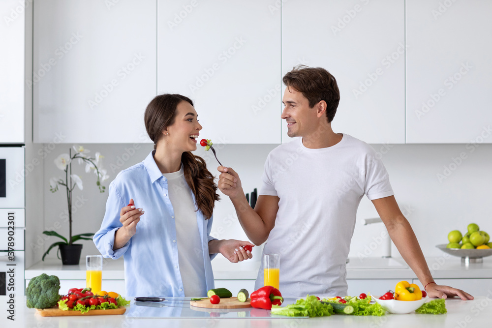 Young couple in love cooking together in the kitchen. Husband feeding wife salad. Young couple in love cooking together in the kitchen. Husband feeding wife salad.