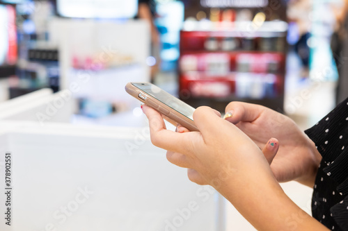 Selective focus at women hand while using smartphone to search for information or get a discount inside department store. Digital coupon that can redeem from mobile device. Technology with business.