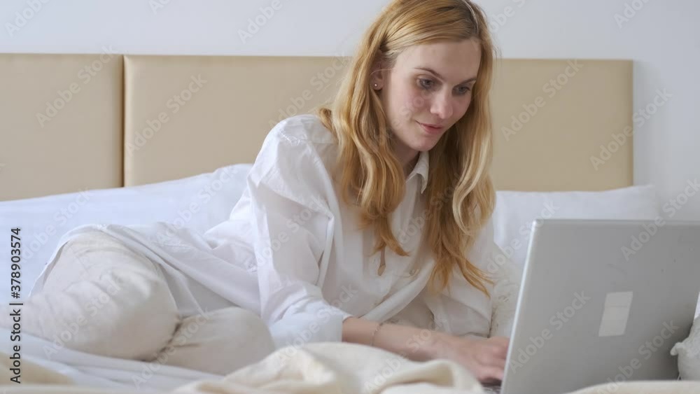 Caucasian woman working behind laptop in bedroom Caucasian woman working behind laptop in bedroom