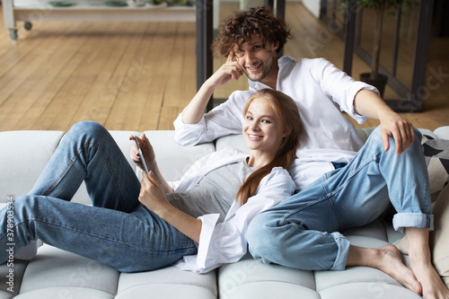 Man and woman relaxing on couch in living room and using digital tablet.