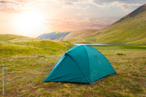 green touristic tent in a mountain valley at the sunset, travel background