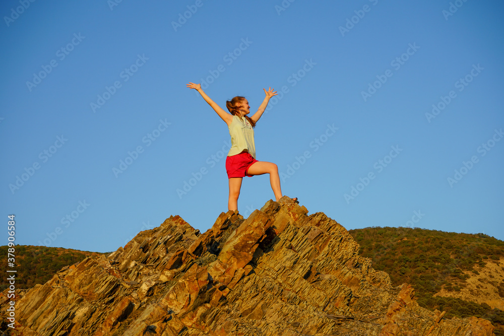 a teenage girl in red shorts and a light green T-shirt stands on a rock and experiences vivid emotions from conquering her first height