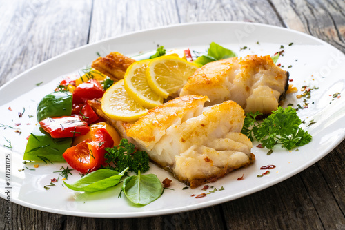 Fish dish - fried cod fillet with fried vegetables and lemon served on wooden table