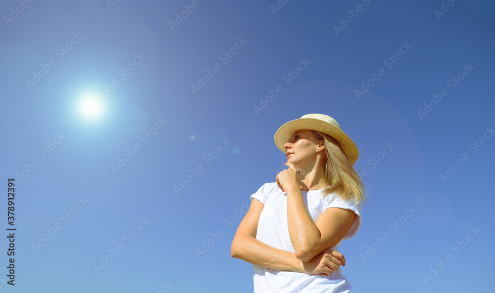 Bottom view of a girl in a hat against a blue sky, the sun is shining