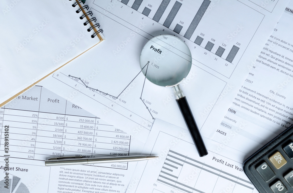Top view of magnifying glass, pen, calculator, notebook and lot of business documents with charts, diagrams and graphs.Concept of researching of financial reports Top view of magnifying glass, pen, calculator, notebook and lot of business documents with charts, diagrams and graphs.Concept of researching of financial reports