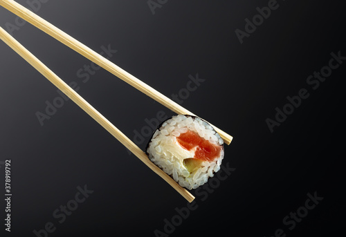 Fresh tasty sushi with wooden chopsticks on a dark background.