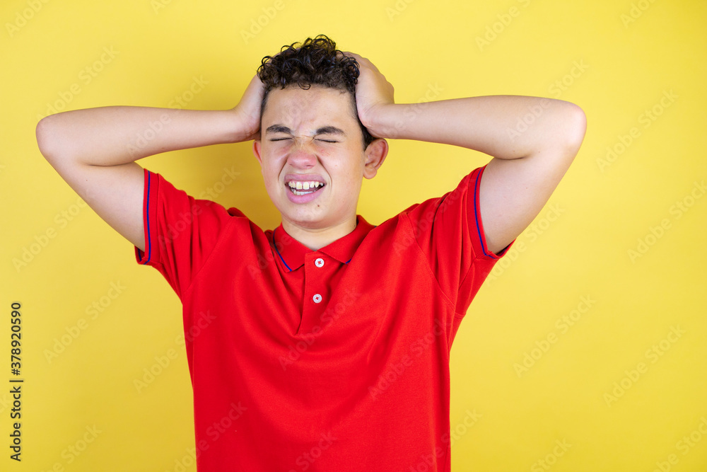 Beautiful teenager boy over isolated yellow background suffering from headache desperate and stressed because pain and migraine with her hands on head Beautiful teenager boy over isolated yellow background suffering from headache desperate and stressed because pain and migraine with her hands on head