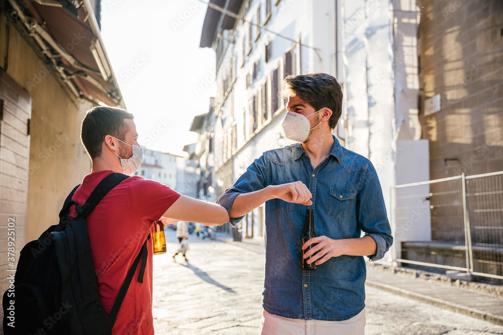 Two young friends meet in the city wearing protective masks from the Corona virus, Covid-19, Millennials greet each other with their arms and elbows protecting themselves from the Coronavirus