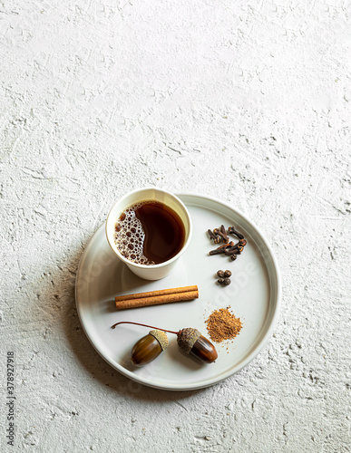 Cardboard cup of acorn coffee and ingredients for delicious acorn coffee  cloves  cinnamon  nutmeg and black pepper on the gray background. Health and no caffeine concept. Flat lay  copy space