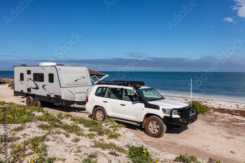 Landscape view of 4WD and modern caravan parked adjacent to a sparkling sunny beach. photo