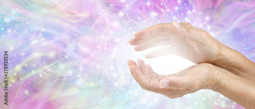 Sensing Awesome Metaphysical Energy Field between hands - female cupped hands with white healing energy against a colourful blue purple green sparkling chaotic background with copy space 
