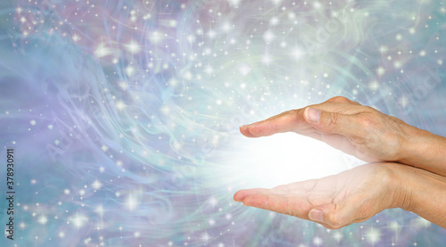 Sending you magical high frequency healing energy - female cupped hands with magical white plasma between flowing sparkles outwards on lilac energy field background with copy space   © Nikki Zalewski