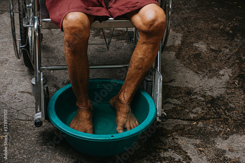Fotografie Asian old man sitting in wheelchair and soak his feet in warm water