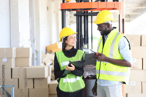 African American and Asian workers wearing safety vest while working in warehouse checking for the inventory with copy space