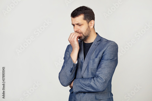 Canvastavla Young businessman with a smile, a man with a beard in a jacket, looks tense and nervous with hands on his lips, biting his nails