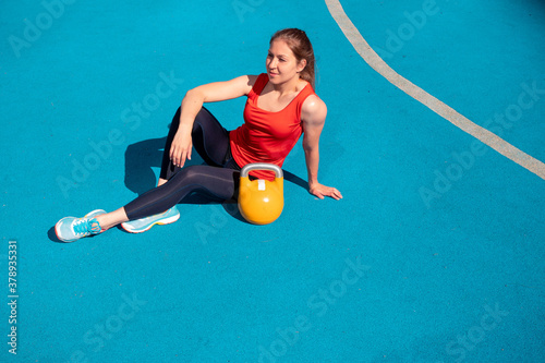 Young female athlete doing workout, training with a kettlebell in the open air. photo