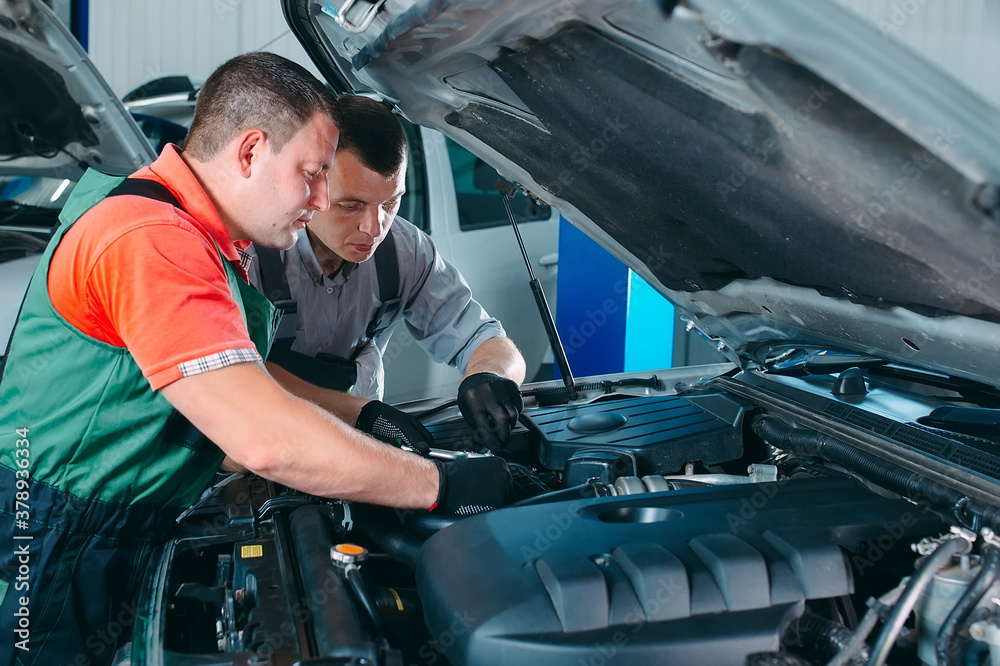 Two handsome mechanics in uniform are working in auto service. Car repair and maintenance. Two handsome mechanics in uniform are working in auto service. Car repair and maintenance.