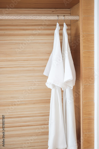 Closeup Fresh white bathrobe hanging in wooden wardrobe at luxury hotel. Relax and travel concept