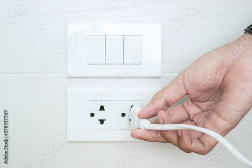 Closeup Male finger unplugging or plugging of electricity device on white wall at home. Energy Saving, power, electrical and lifestyle concepts