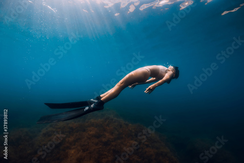 Freediver glides with fins under sea. Woman is doing freediving in the sea