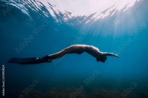 Freediver glides with fins under sea. Woman is doing freediving in sea