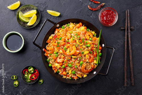 Stir fry rice with vegetables and shrimps in black iron pan. Slate background. Close up. Top view.